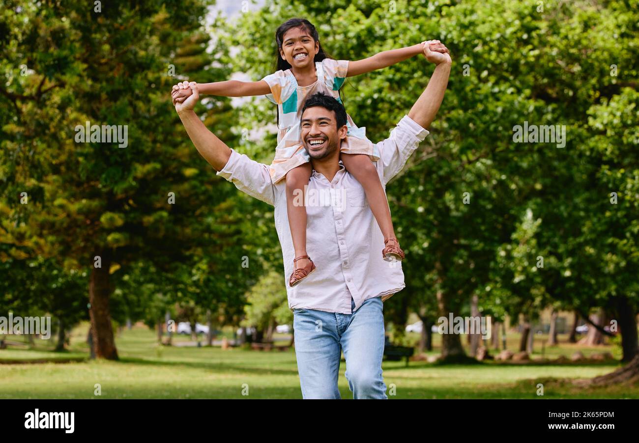 Glücklich asiatische alleinerziehenden Vater trägt Tochter auf seinen Schultern im Park. Lächelnder Mann und Kind geben vor, dass sie mit ausgestreckten Armen fliegen können Stockfoto