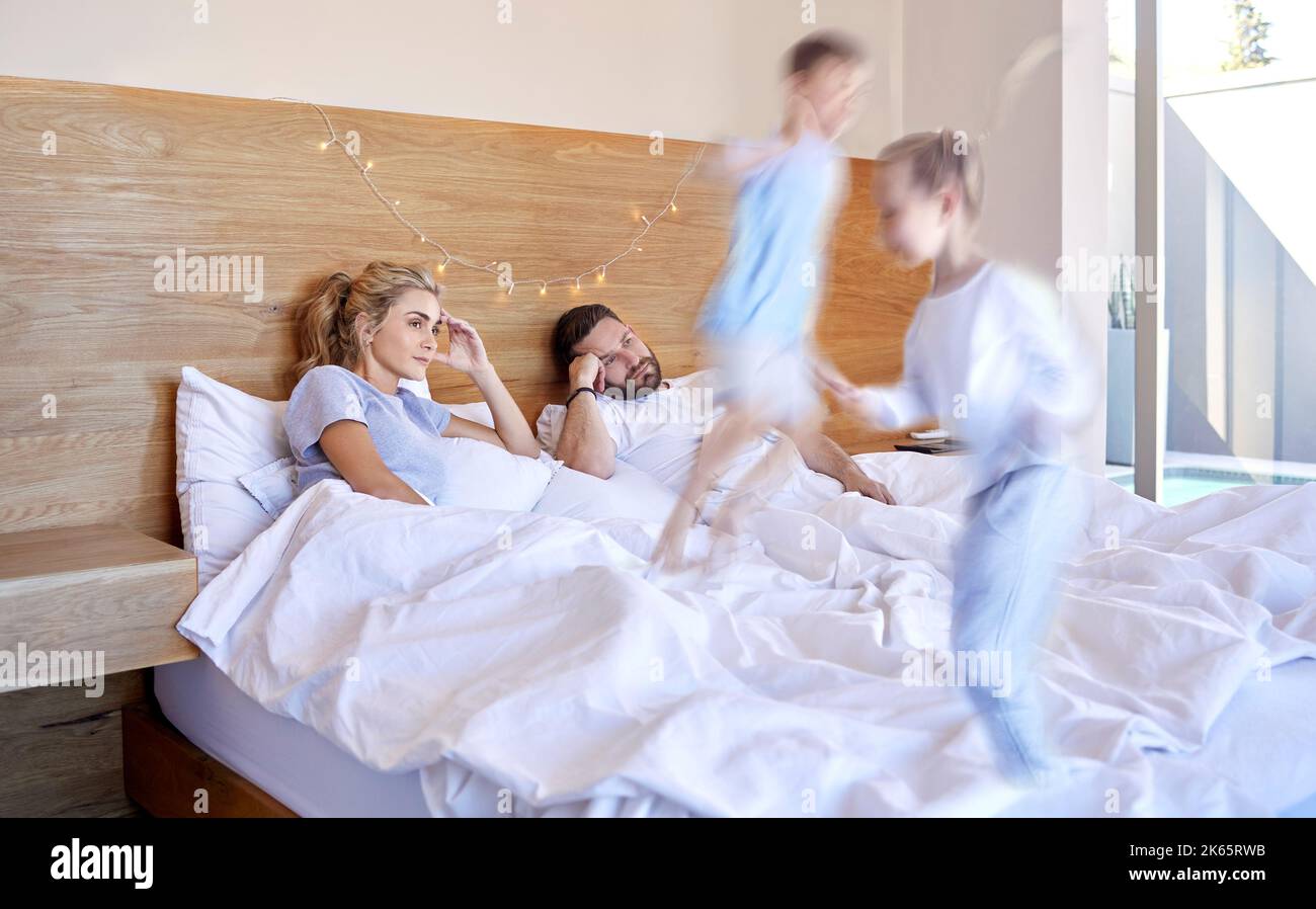 Müde und gestresste Eltern, die unter Kopfschmerzen leiden, während adhd-Kinder zu Hause auf das Bett springen. Laute, freche Geschwister ärgern ihre Mutter und ihren Vater Stockfoto
