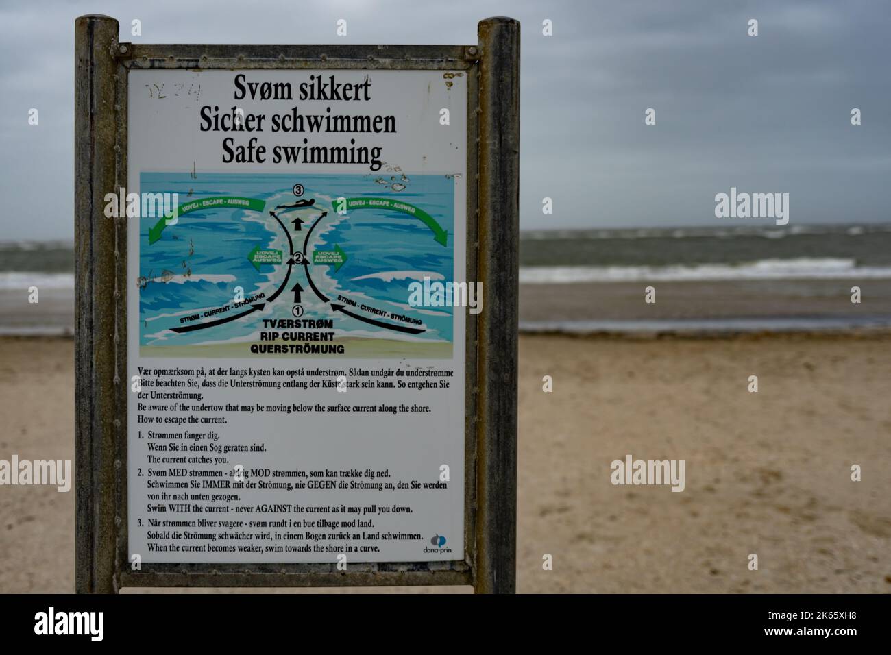 Ein Warnschild an einem einsamen Strand bei schlechtem Wetter weist auf die Gefahr für Schwimmer hin Stockfoto