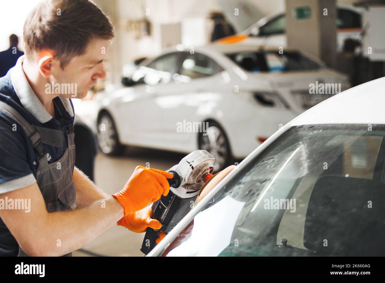 Fahrzeugdetails. Man arbeitet mit Orbitalpolierer und poliert weißes Auto, Nahaufnahme. Stockfoto