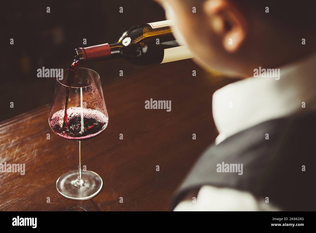 Nahaufnahme, Sommelier gießt Rotwein ins Glas auf der Theke Hintergrund. Stockfoto