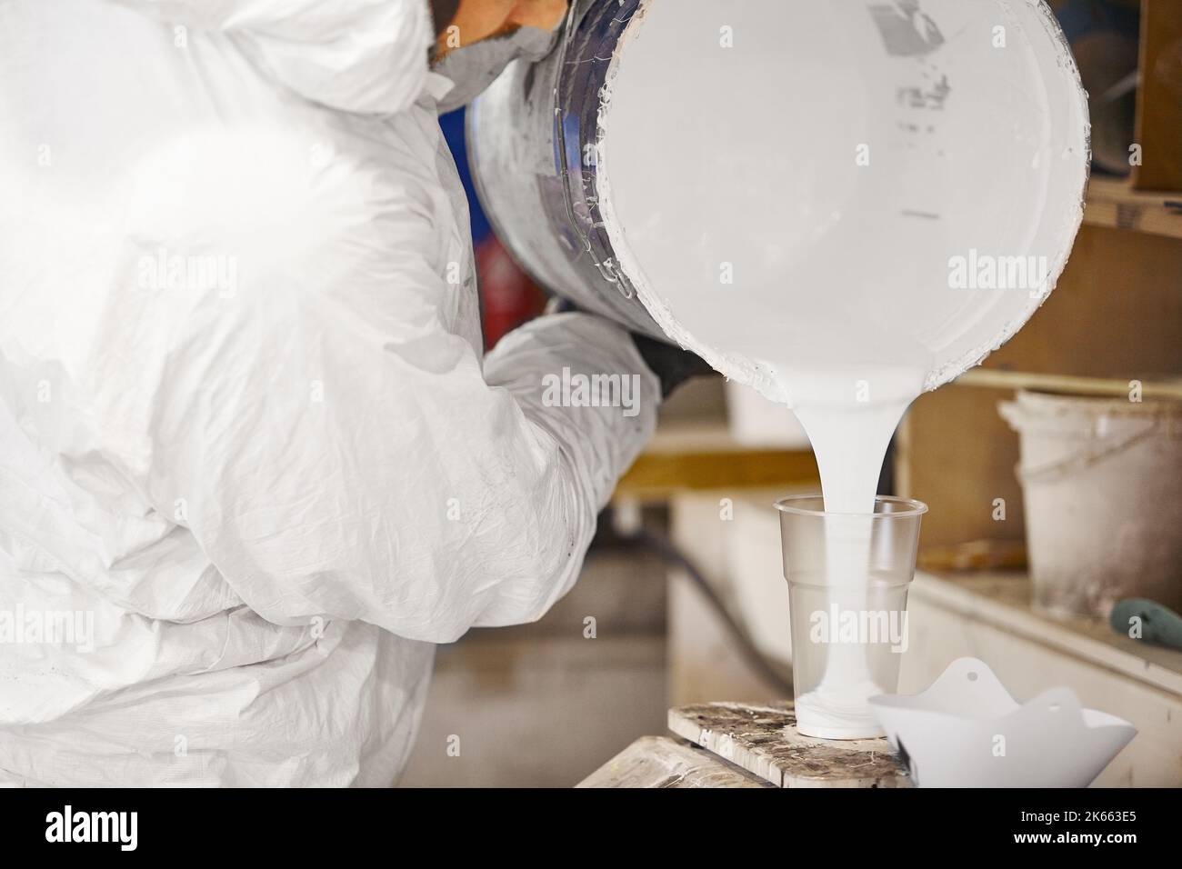 Der Mann gießt dosierte Menge Farbe in einen Plastikbecher. Stockfoto