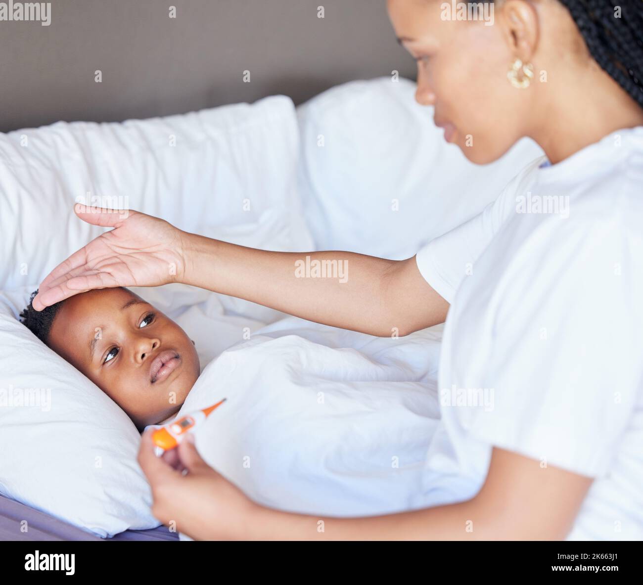 afroamerikanische Frau, die ihren Sohn temperiert. Mutter verwendet Thermometer, um die Sons-Temperatur zu messen. Kranker kleiner Junge liegt im Bett. Besorgt Stockfoto