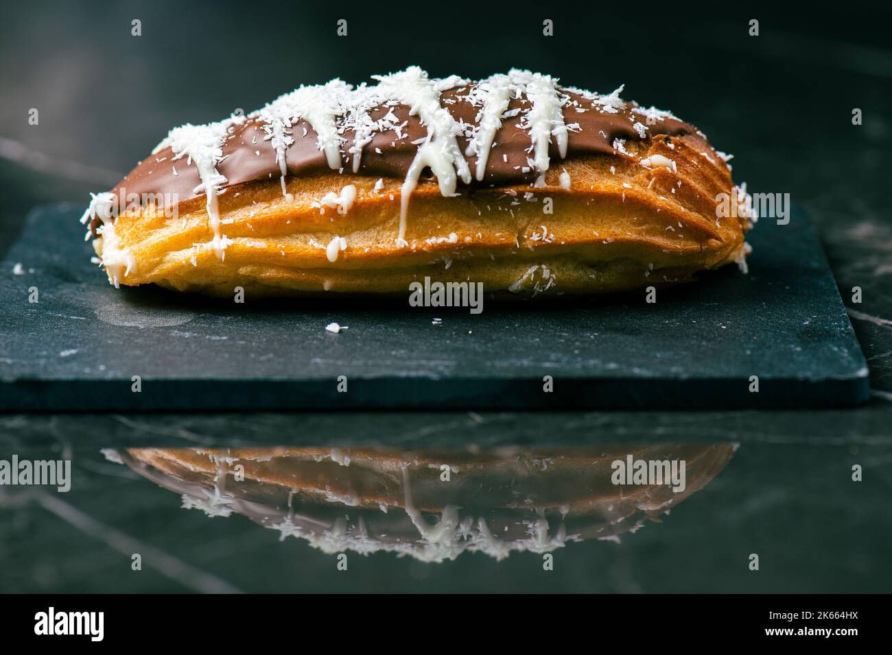 Hausgemachtes Eclair mit Mango- und Kokosnuss-Schlagsahne. In Milchschokolade getaucht. Stockfoto