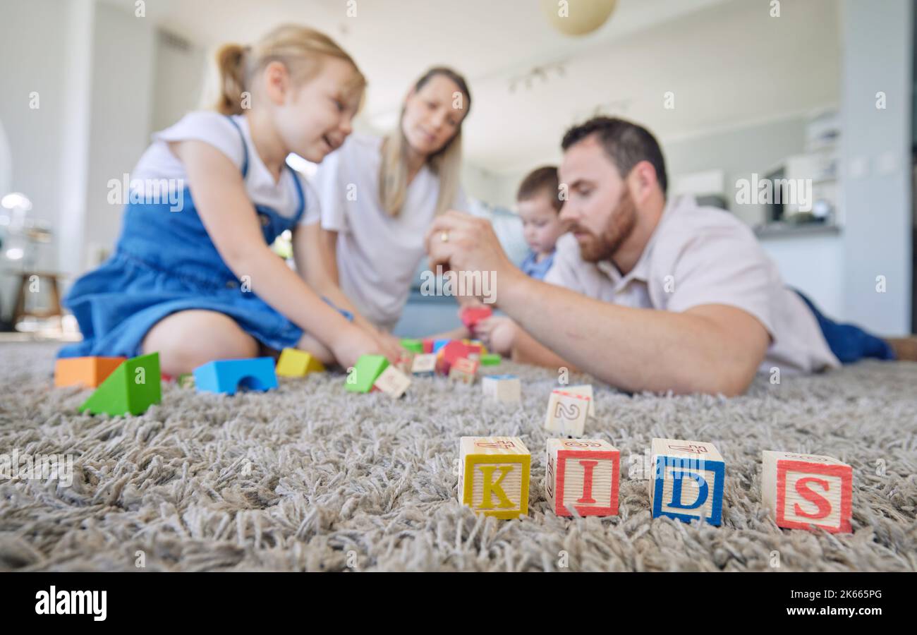 Kaukasische vierköpfige Familie, die mit Spielzeug spielt und zu Hause in der Lounge auf dem Boden sitzt. Eltern verbringen Zeit mit ihren kleinen Kindern Stockfoto