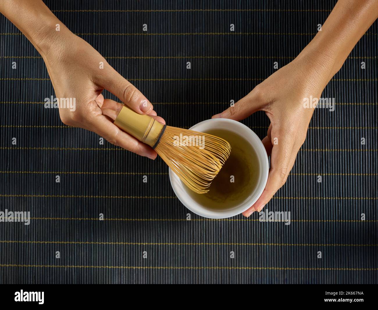 Hände, die Matcha-Tee in einer weißen Schüssel mit einem Bambusbesen zubereiten Stockfoto
