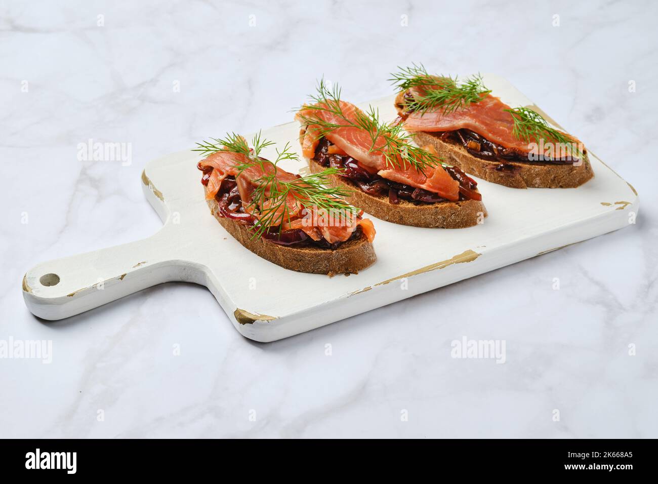 Lachs-Sandwich mit karamellisierten Zwiebeln auf einem hölzernen Servierbrett Stockfoto