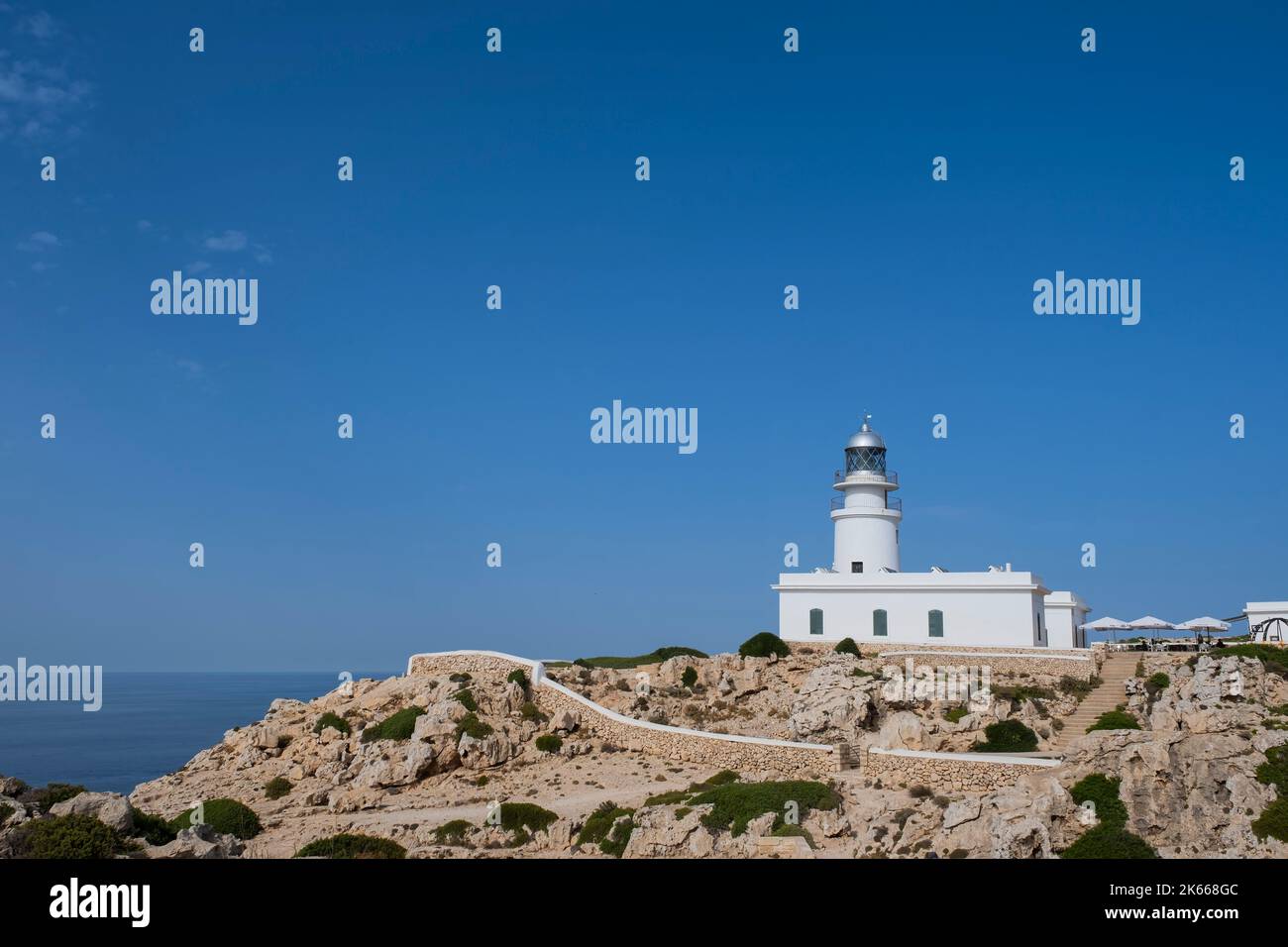 Weißer Leuchtturm auf einer felsigen Klippe mit weißen Mauern umgeben und das Meer im Hintergrund, Cavalleria Cape Leuchtturm, Fornells, Menorca Stockfoto