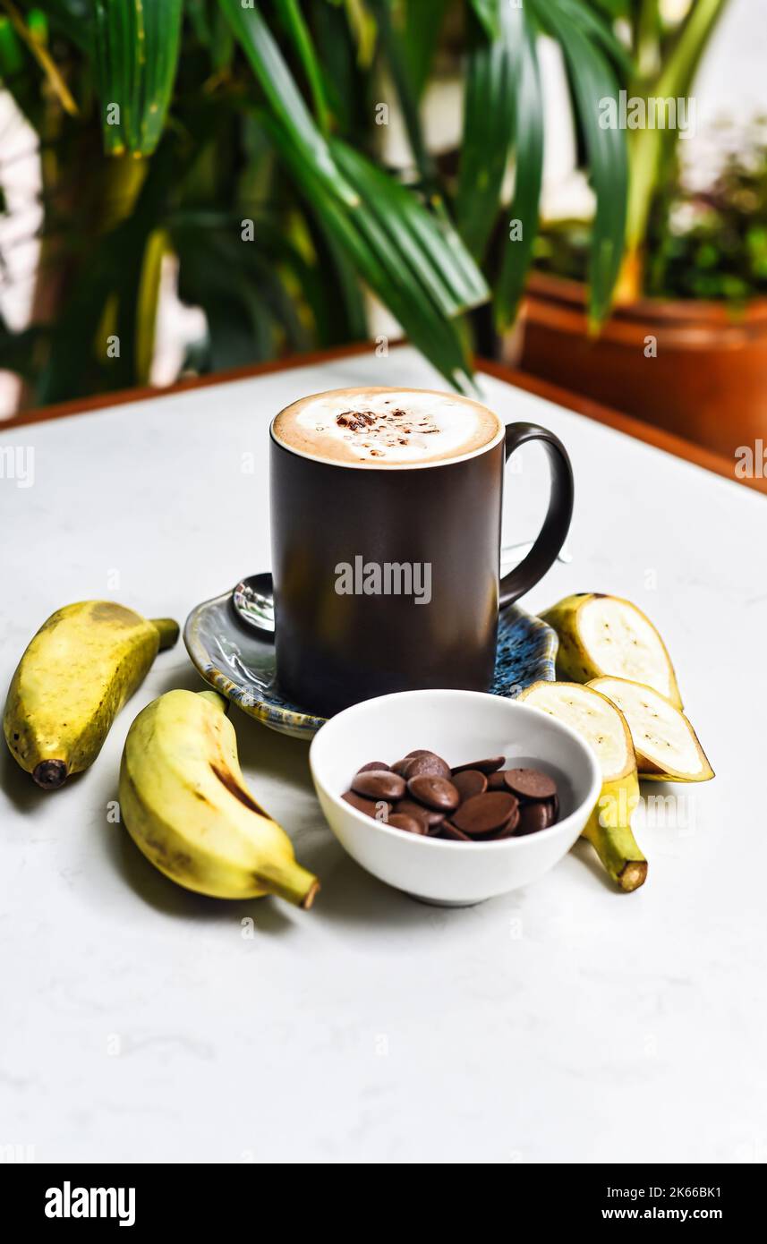 Bananenschokolade-Latte mit frischen Bananen- und Schokoladentropfen auf weißem Tisch Stockfoto