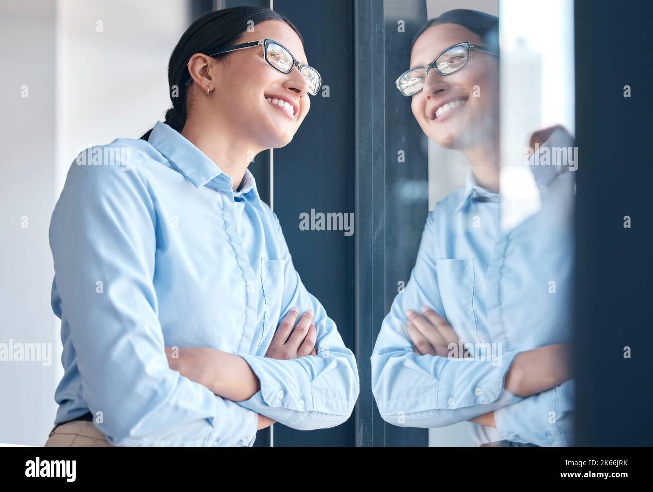 Selbstbewusste, ermächtigte Geschäftsfrau mit gemischter Rasse, die eine Brille trägt und mit gekreuzten Armen aus einem Fenster blickt. Eine Frau nur denken und Stockfoto