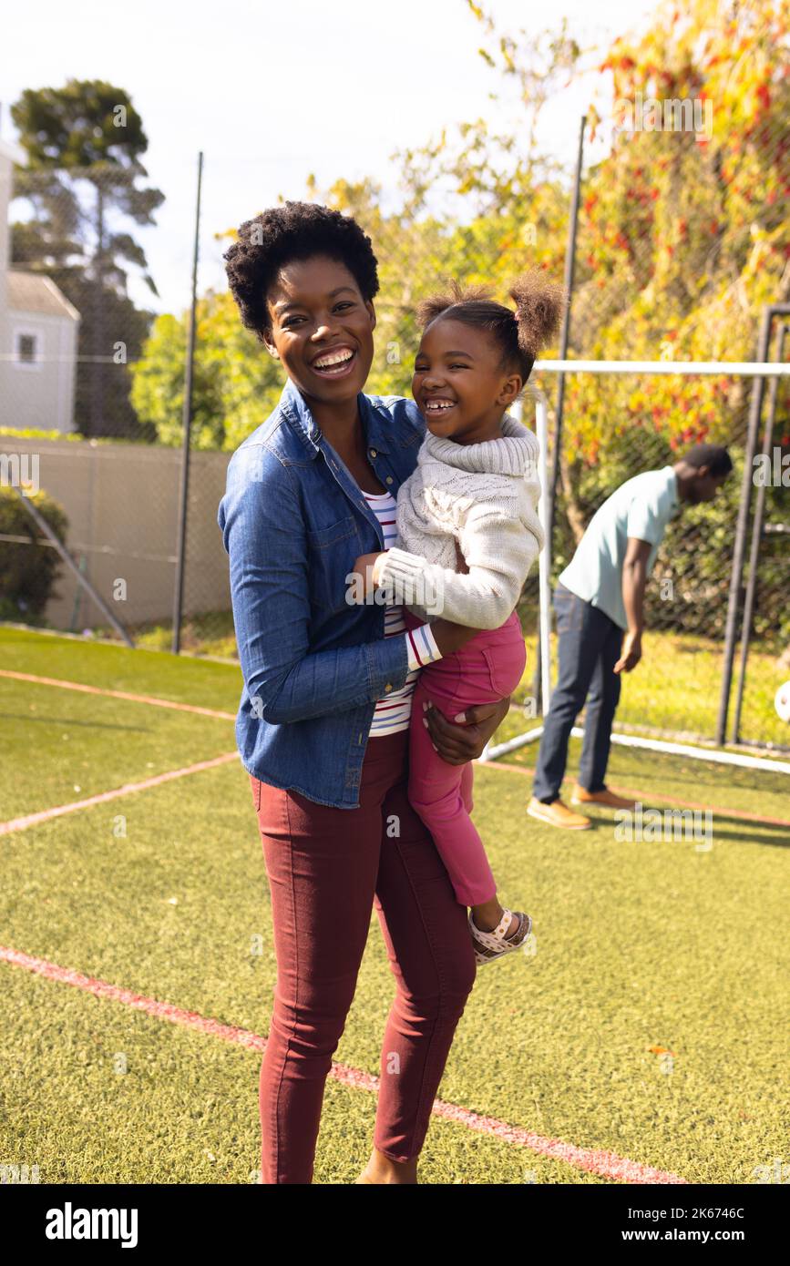 Glückliche afroamerikanische Mutter und Tochter, die Zeit zusammen verbringen und draußen Football spielen Stockfoto