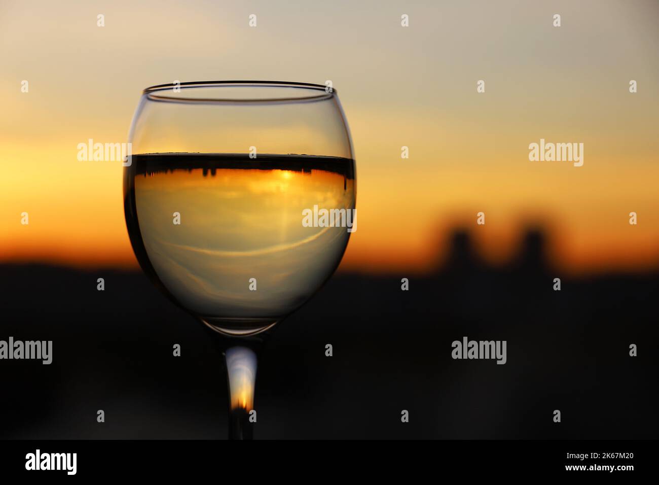 Weinglas mit Stadtgebäuden, die auf dem Hintergrund des Sonnenuntergangs reflektiert werden. Konzept der Feier, Weinindustrie Stockfoto