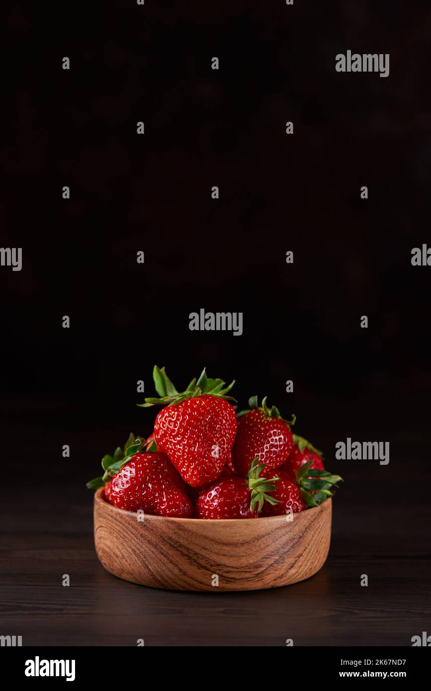 Frische Erdbeeren in einer Holzschale auf braunem Hintergrund. Vertikal, Kopierbereich, Nahaufnahme. Stockfoto