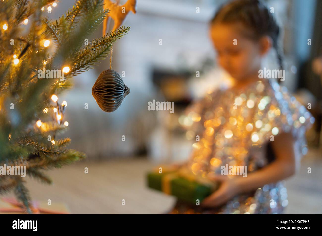 Frohe Feiertage. Kleines Kind öffnet Geschenk in der Nähe von Weihnachtsbaum. Das Mädchen lacht und genießt das Geschenk. Stockfoto