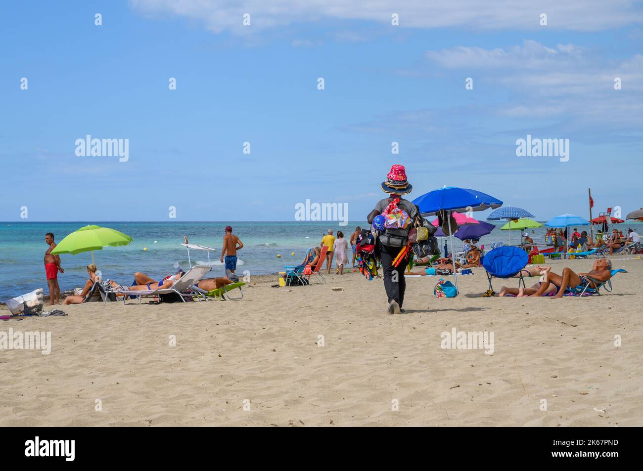 Ein schwarzer afrikanischer Strandverkäufer läuft am Ende der Saison unter Sonnenanbetern, die versuchen, seine Waren am Fontanelle-Strand in Apulien, Italien, zu verkaufen. Stockfoto