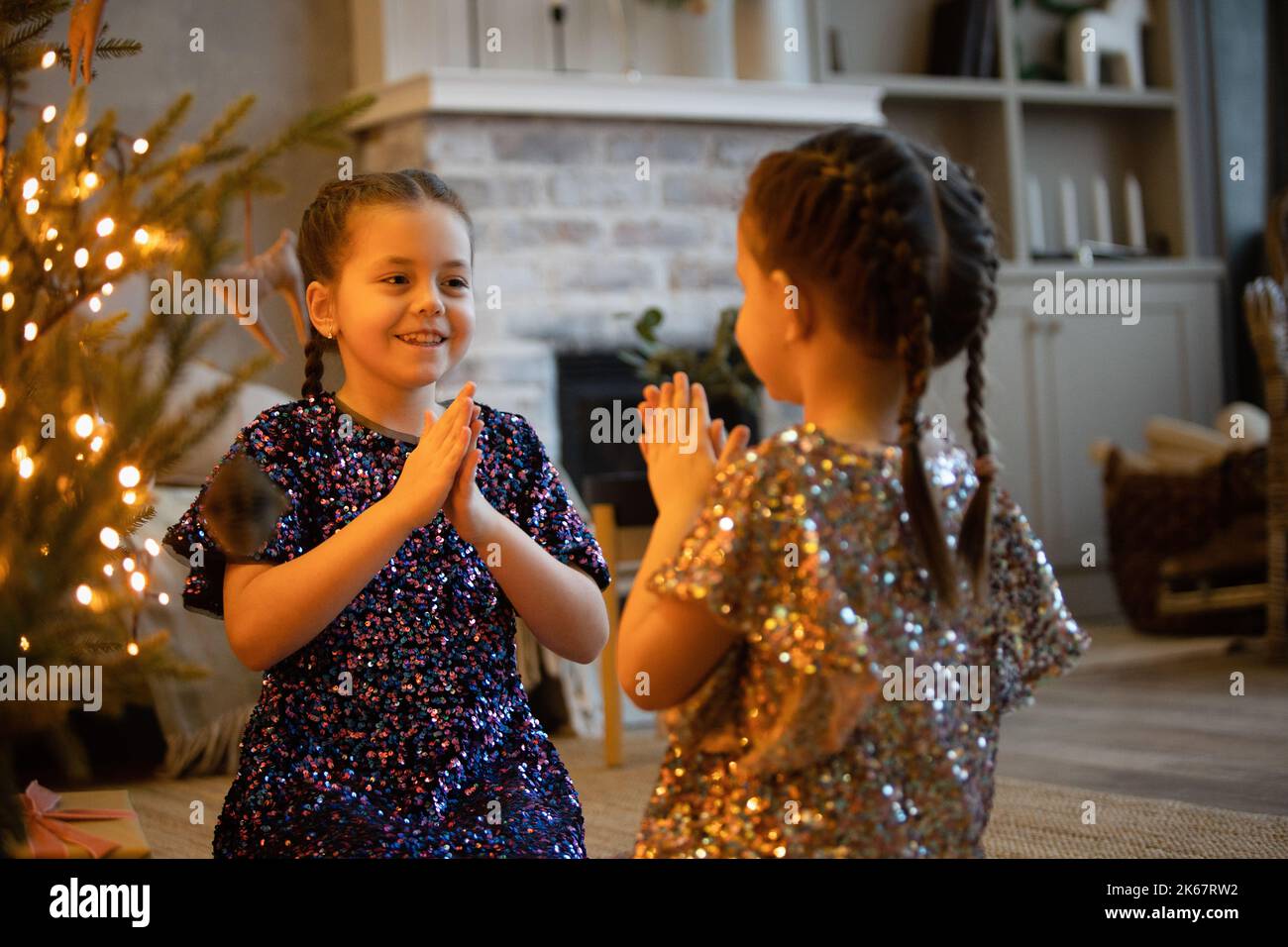 Zwei Schwestern spielen in der Nähe des Weihnachtsbaums und Geschenke. Mädchen schauen sich an und lachen in der Nähe des Weihnachtsbaums. Stockfoto