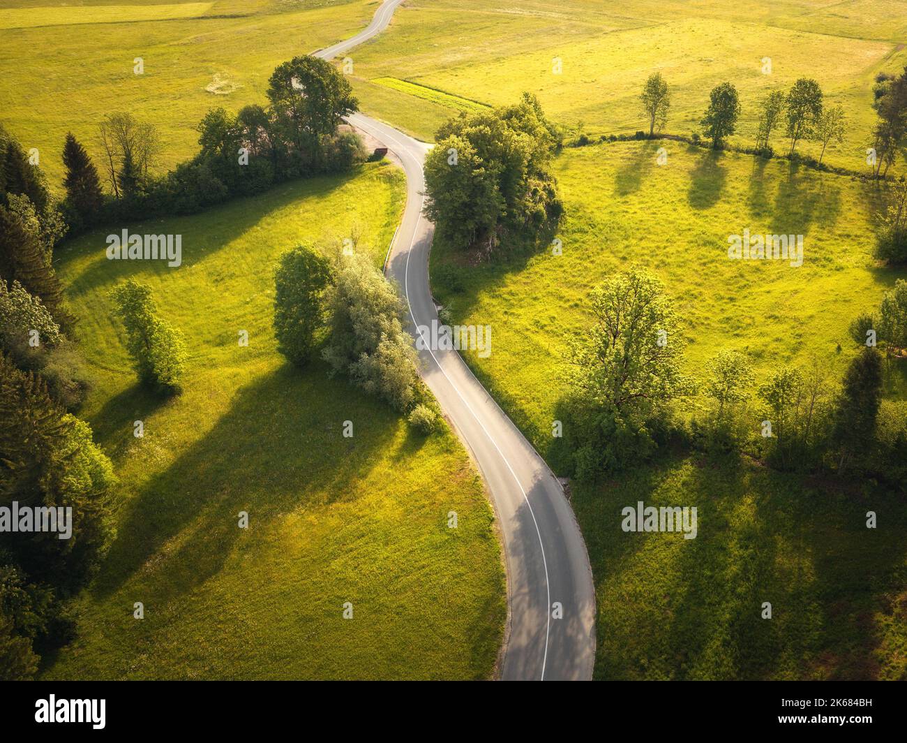 Luftaufnahme der Straße in grünen Wiesen und Hügeln bei Sonnenuntergang im Sommer Stockfoto