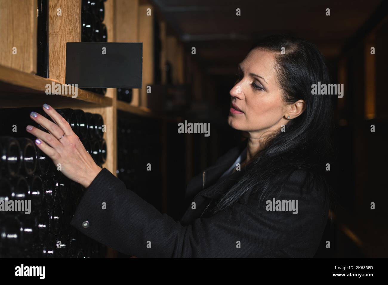 Frau, die Weinflaschen, Jahrgang 2006, aus einem Weinregal in einem benutzerdefinierten Weinkeller nimmt Stockfoto