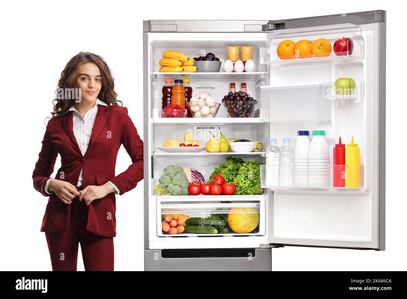 Junge professionelle Frau, die sich auf einen Kühlschrank stützt und das Essen auf weißem Hintergrund isoliert hat Stockfoto