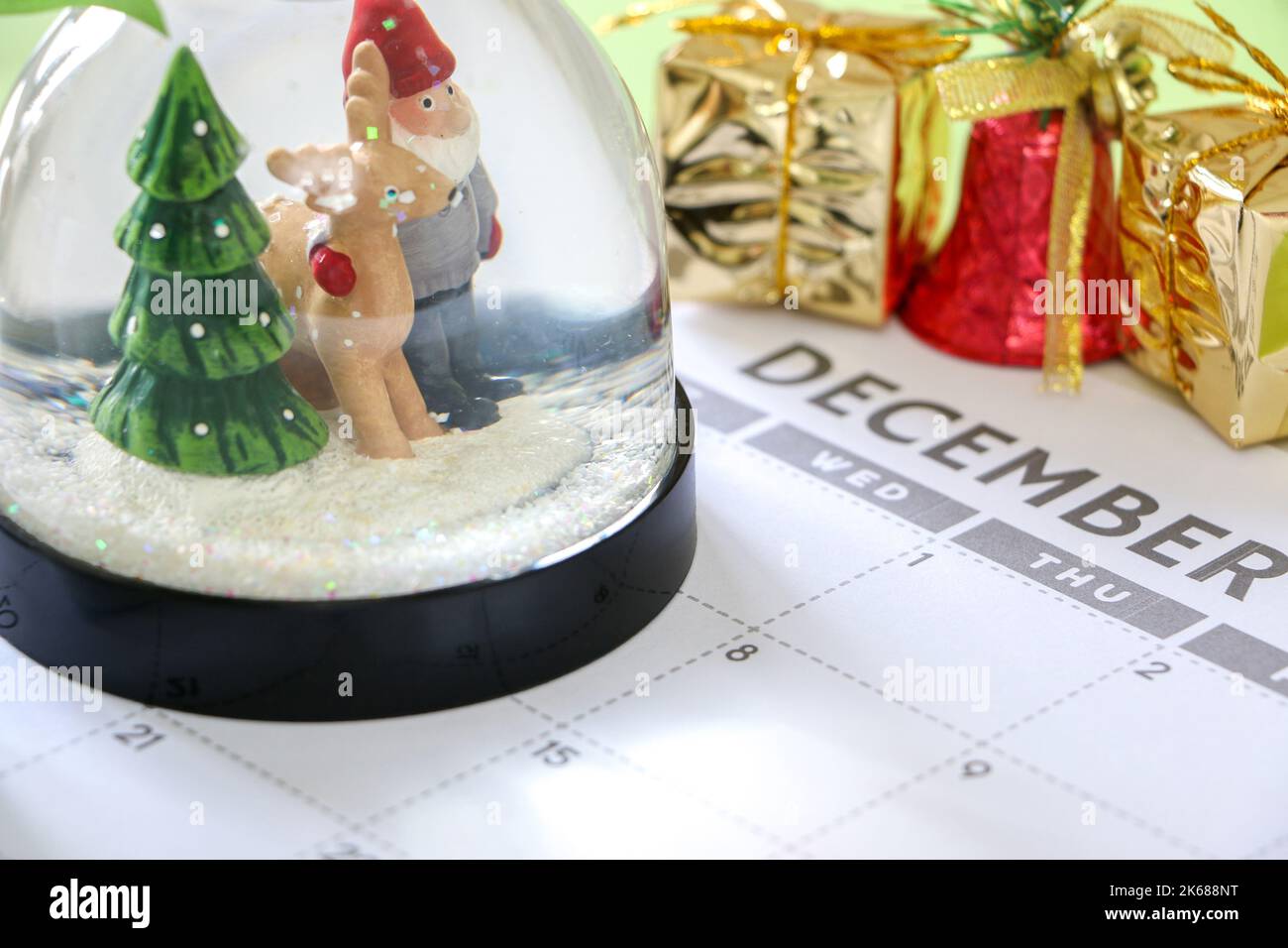 Countdown bis Weihnachten, festliche Schneekugel im Dezember-Kalender, Weihnachtsdekorationen wie Geschenke und Glocken im Hintergrund Stockfoto