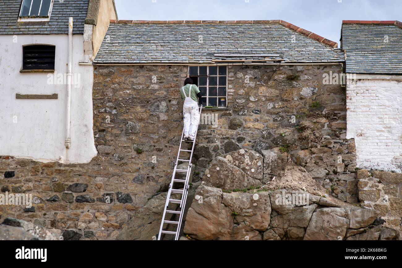 Ein Mann auf einer Leiter repariert ein kaputtes Fenster in einem alten Steinhaus Stockfoto