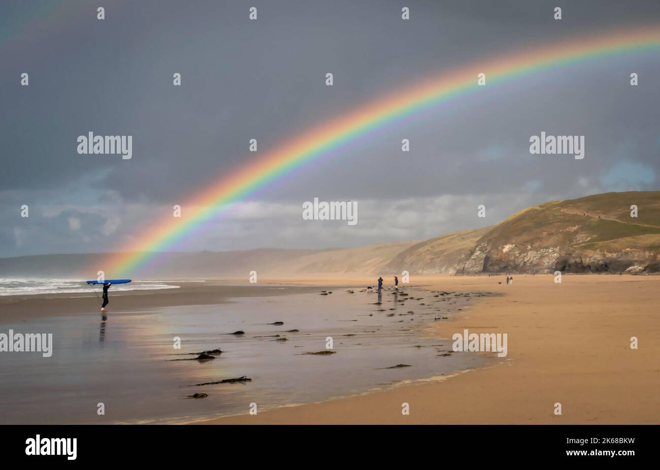 Ein Surfer in Cornwall, der von einem Regenbogen beleuchtet wird Stockfoto