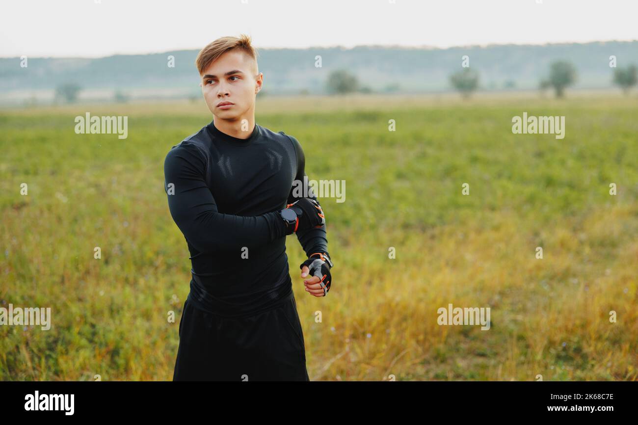 Ein junger Mann, der während der goldenen Stunde im Wald trainiert, den Puls streckt und misst, während er die Natur genießt Stockfoto