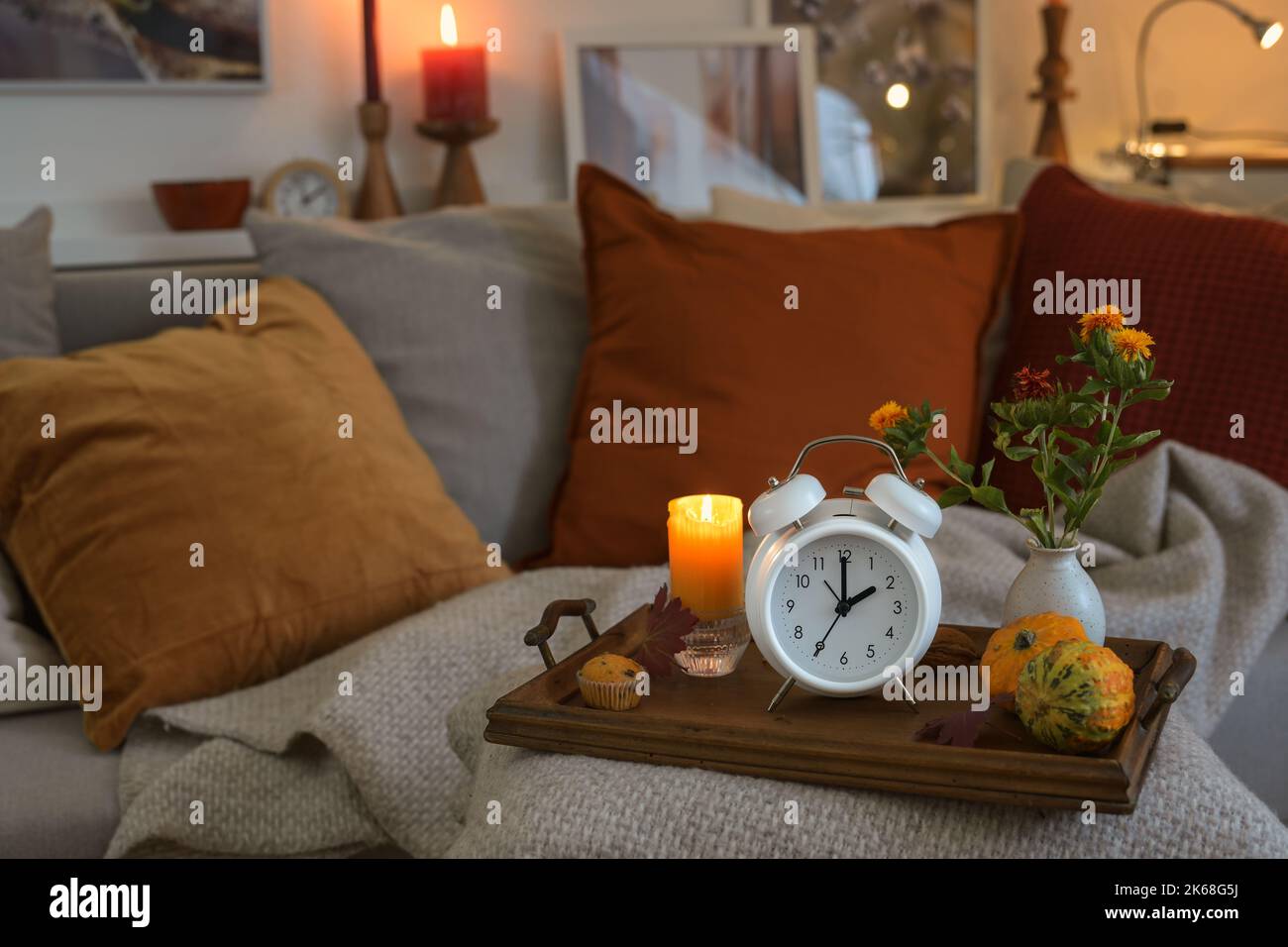 Weißer Vintage-Wecker mit Herbstrückfallzeit nach der Sommerzeit, Holztablett mit Kerze und warm gefärbter Herbstdekoration auf einer c Stockfoto