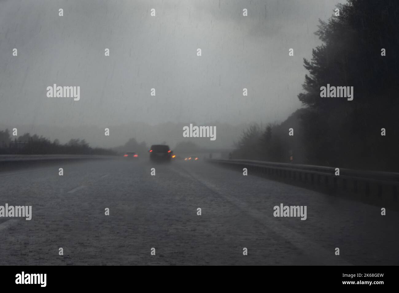 Starker Regen auf der Autobahn, verschwommene Autos mit roten Schlussleuchten, Tropfen und Wasser auf der dunklen Straße, gefährliches Wetter während der Fahrt, Verkehr und Transport Stockfoto