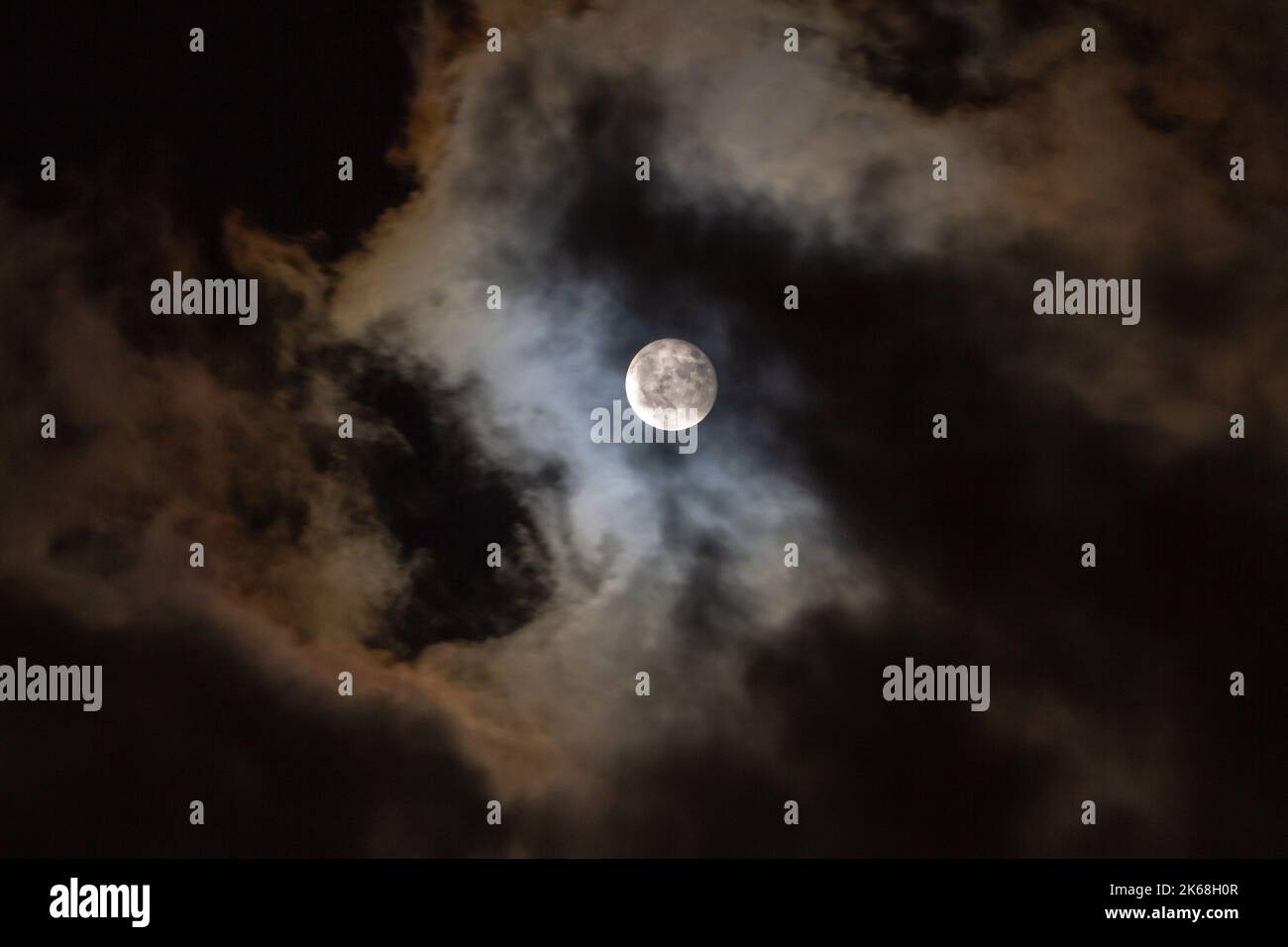 Bunte Wolken ziehen vor einem Vollmond am Nachthimmel vorbei. Stockfoto