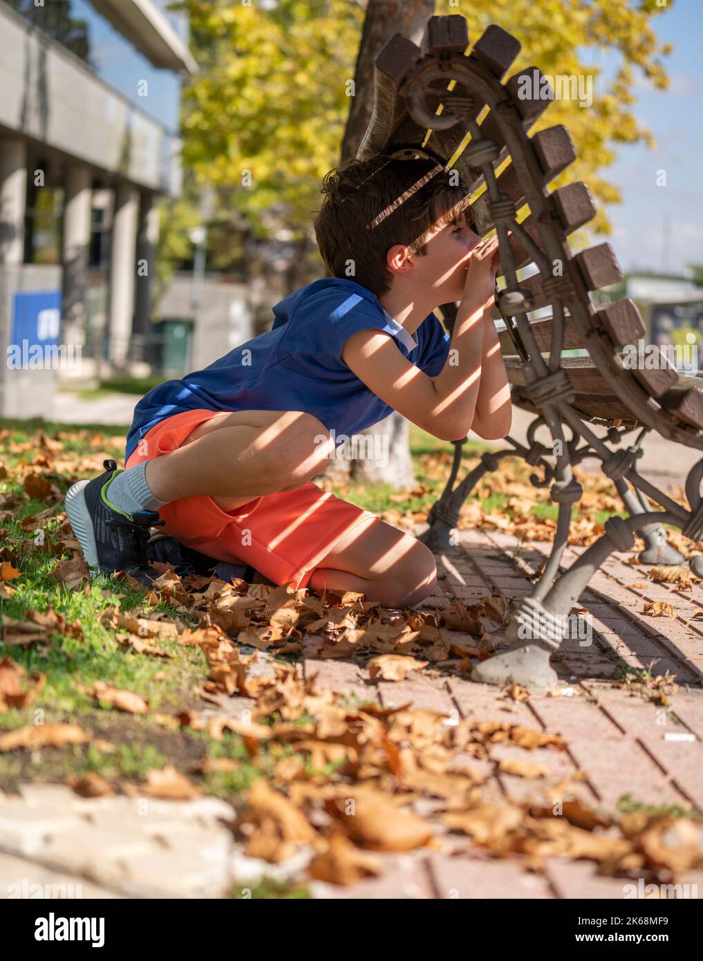 Junge spielt Verstecken und suchen. Blick durch eine Lücke in einer hölzernen Parkbank Stockfoto
