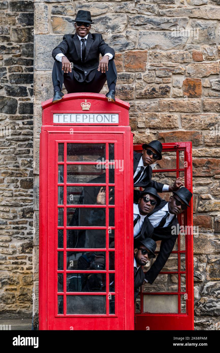 Die akrobatische Gruppe der Black Blues Brothers treten im Dean Village an einer roten Telefonbox auf, Edinburgh, Schottland, Großbritannien Stockfoto