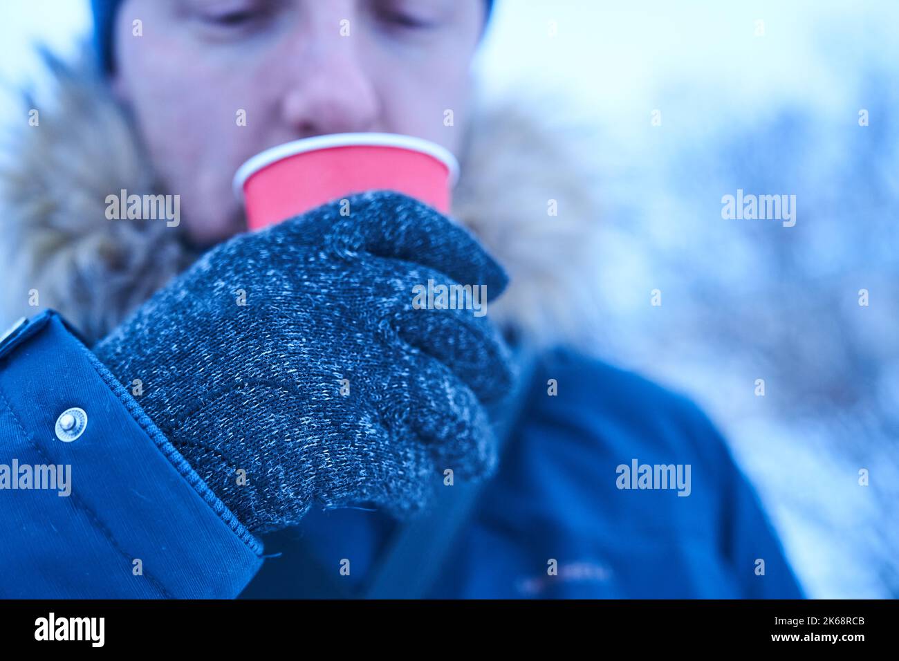 Ein Mann trinkt im Winter draußen ein heißes Getränk aus einer Papiertasse, kaltes Winterwetter mit heißem Tee, die Hand eines Mannes in Handschuhen. Hochwertige Fotos Stockfoto