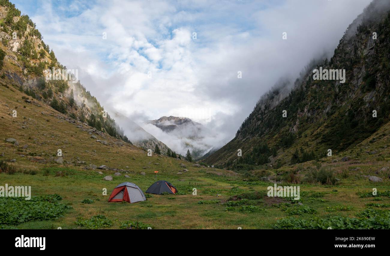 Malerische Berglandschaft mit Zelten. Dramatische alpine Landschaft mit zwei Zelten auf Gras im grünen Bergtal bei nebligen Wetter. Stockfoto