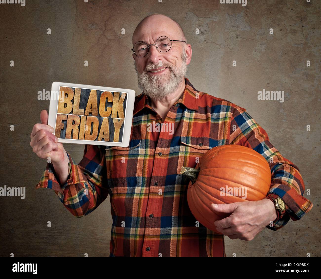 Schwarzes Freitagsschild - lächelnder und fröhlicher Senior mit einem großen Kürbis und einem digitalen Tablet mit Text in Buchdruckholzart, Herbstferien Shopping Stockfoto