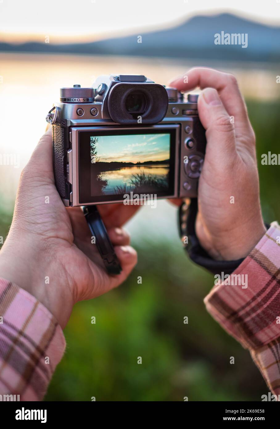 Hand hält eine spiegellose Digitalkamera Vorbereitung für ein Landschaftsfoto. Hände, die den Sonnenuntergang mit der Kamera spiegellos fotografieren. Hand-Grap-Kamera Stockfoto