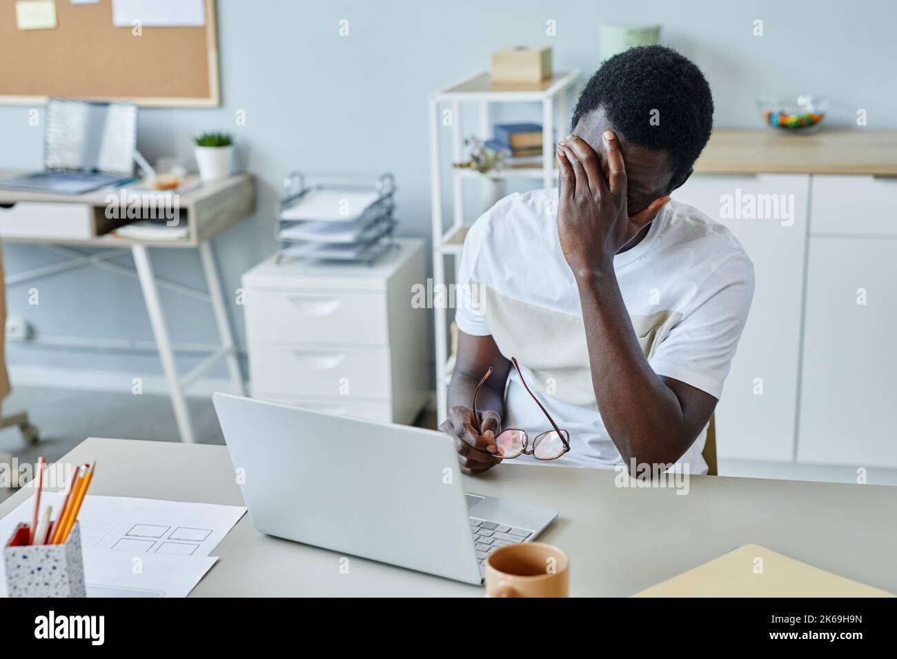 Porträt eines frustrierten schwarzen Mannes am Arbeitsplatz, der die Brille auszieht und unter Kopfschmerzen leidet Stockfoto