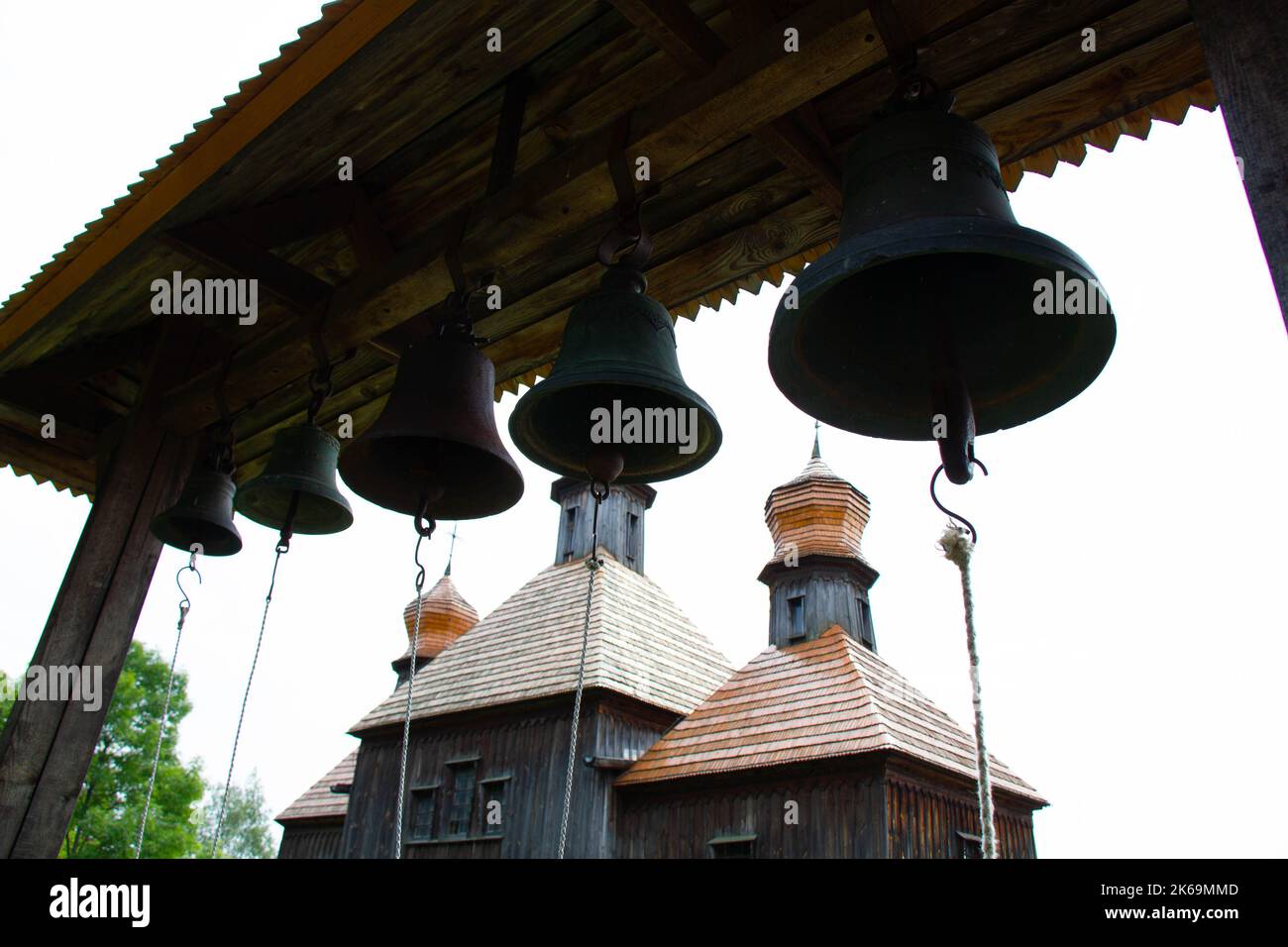 Glocken in der Nähe der Kirche. Massive gusseiserne Gebetsglocken vor dem Hintergrund einer christlich-orthodoxen Holzkirche. Alte katholische Kirche Stockfoto