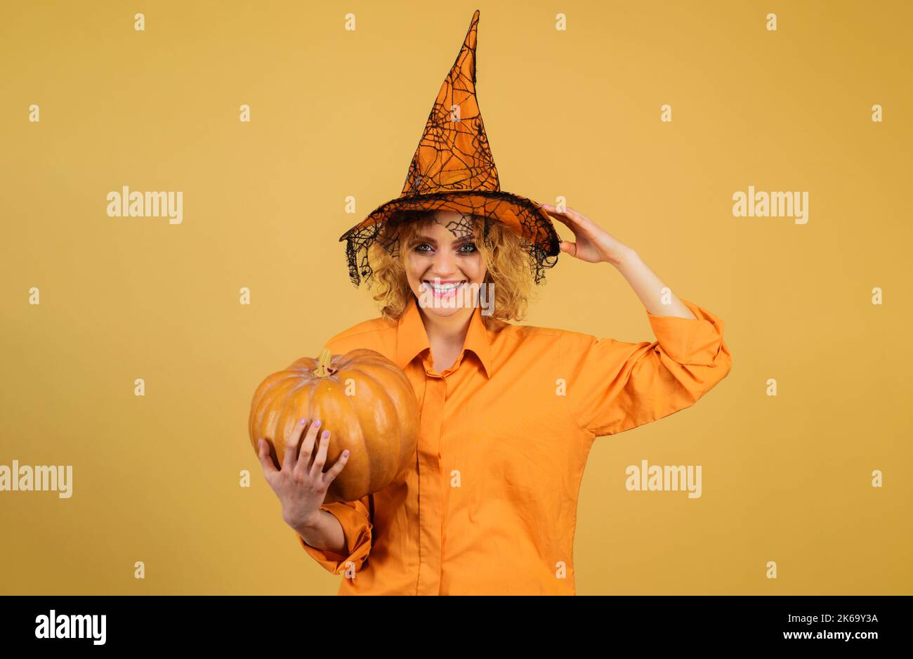 Halloween Party Mädchen mit Kürbis. Lächelnde Frau im Hexenhut mit Jack-o-Laterne. Stockfoto
