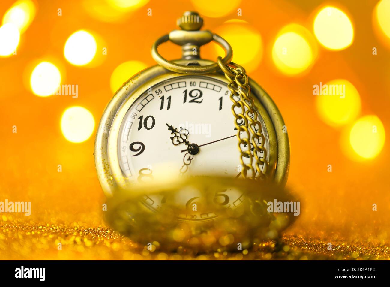Weihnachten und Neujahr.Goldene Uhr in Gold Glitter auf einem gelben Hintergrund mit leuchtenden Bokeh.Weihnachtszeit.Weihnachts-Tapete.Feiertagsbeleuchtung Stockfoto