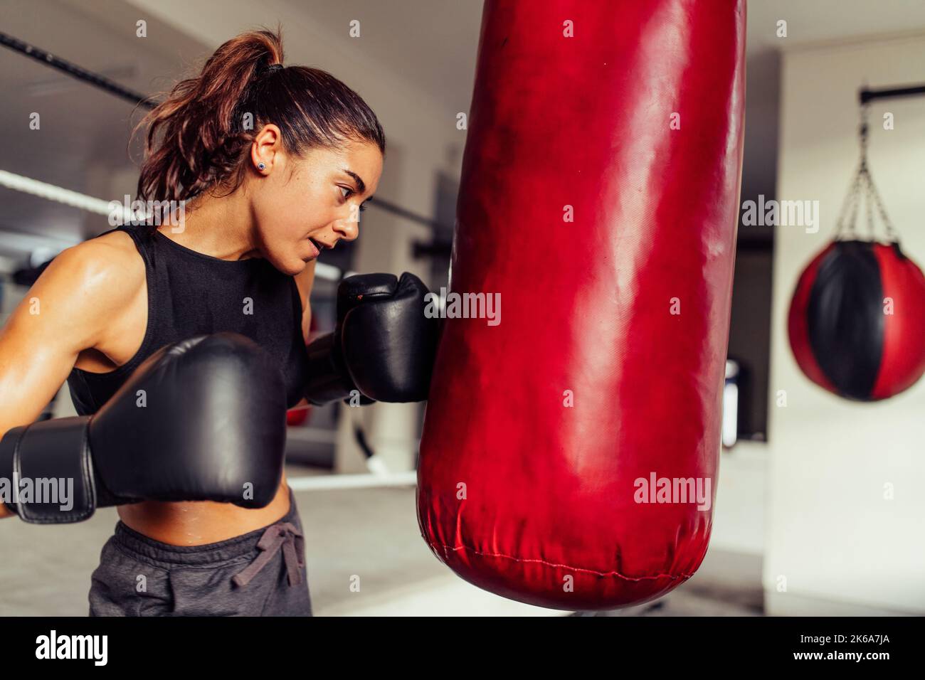 Entschlossene Boxerin, die beim Training im Fitnessstudio einen roten Beutel sticht. Athletische junge Frau, die ihre Schlagtechniken in einer Boxhalle übt. Stockfoto