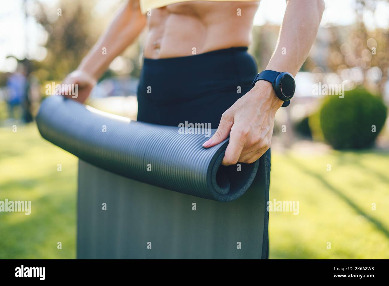 Reife Hände einer Frau, die auf dem Gras eines grünen Parks eine Yoga-Matte entfaltet und Sportkleidung trägt. Naturkonzept. Gesundes Lifestyle-Konzept. Natürlich Stockfoto