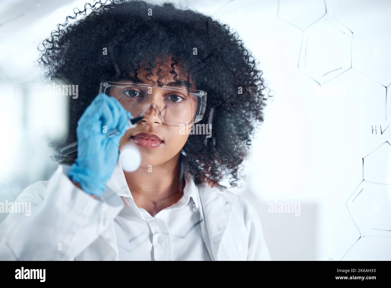 Fokussierter junger Wissenschaftler beim Brainstorming, Gedanken an Ideen im Labor. Die junge Chemikerin arbeitet an ihrer Forschungsformel und schreibt auf einem Brett. Weiblich Stockfoto