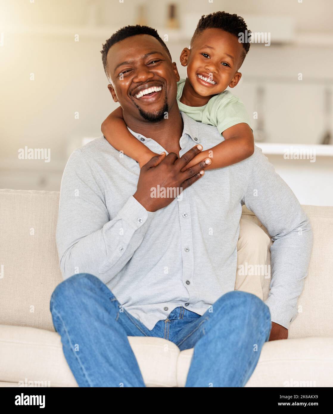 Porträt eines liebevollen schwarzen Mannes, der sein Kind auf einer Couch hält. afroamerikanischer Vater, der sich zu Hause mit seinem Sohn verbunden hat. Schwarzer alleinerziehender Vater lachend Stockfoto