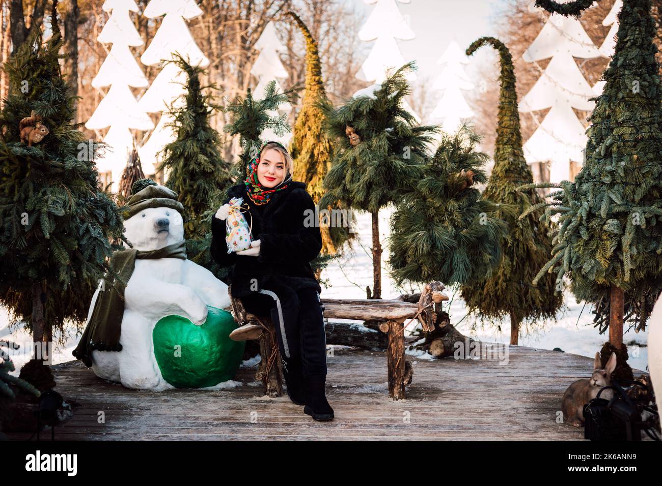 Eine Frau in einem nationalen ukrainischen Kopftuch sitzt auf einer Bank in der Nähe von Weihnachtsbäumen Stockfoto
