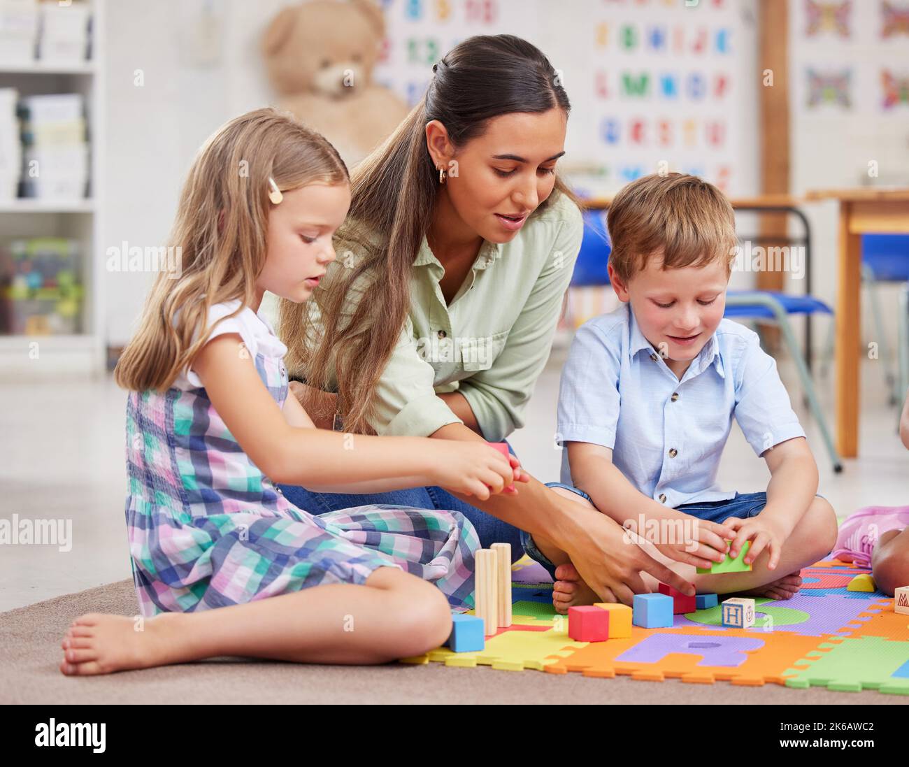 Eine junge Frau, die eine Klasse von Kindern im Vorschulalter unterrichtet, sonnt sich in der Herrlichkeit von Spielzeug und Puzzles. Stockfoto
