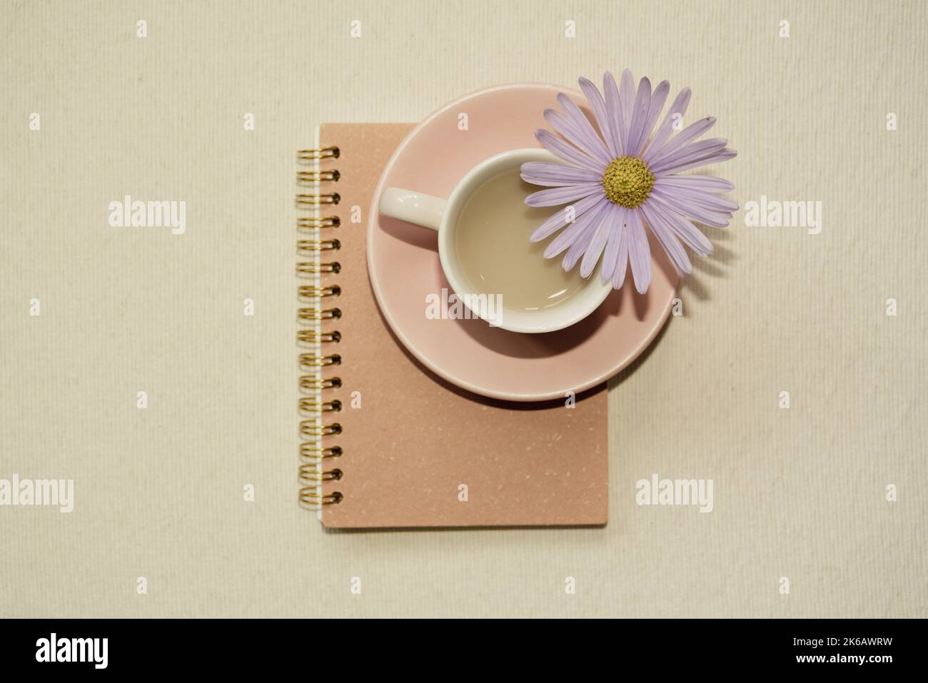 Rosafarbene Tasse Kaffee und Notizbuch auf dem Schreibtisch. Draufsicht Stockfoto
