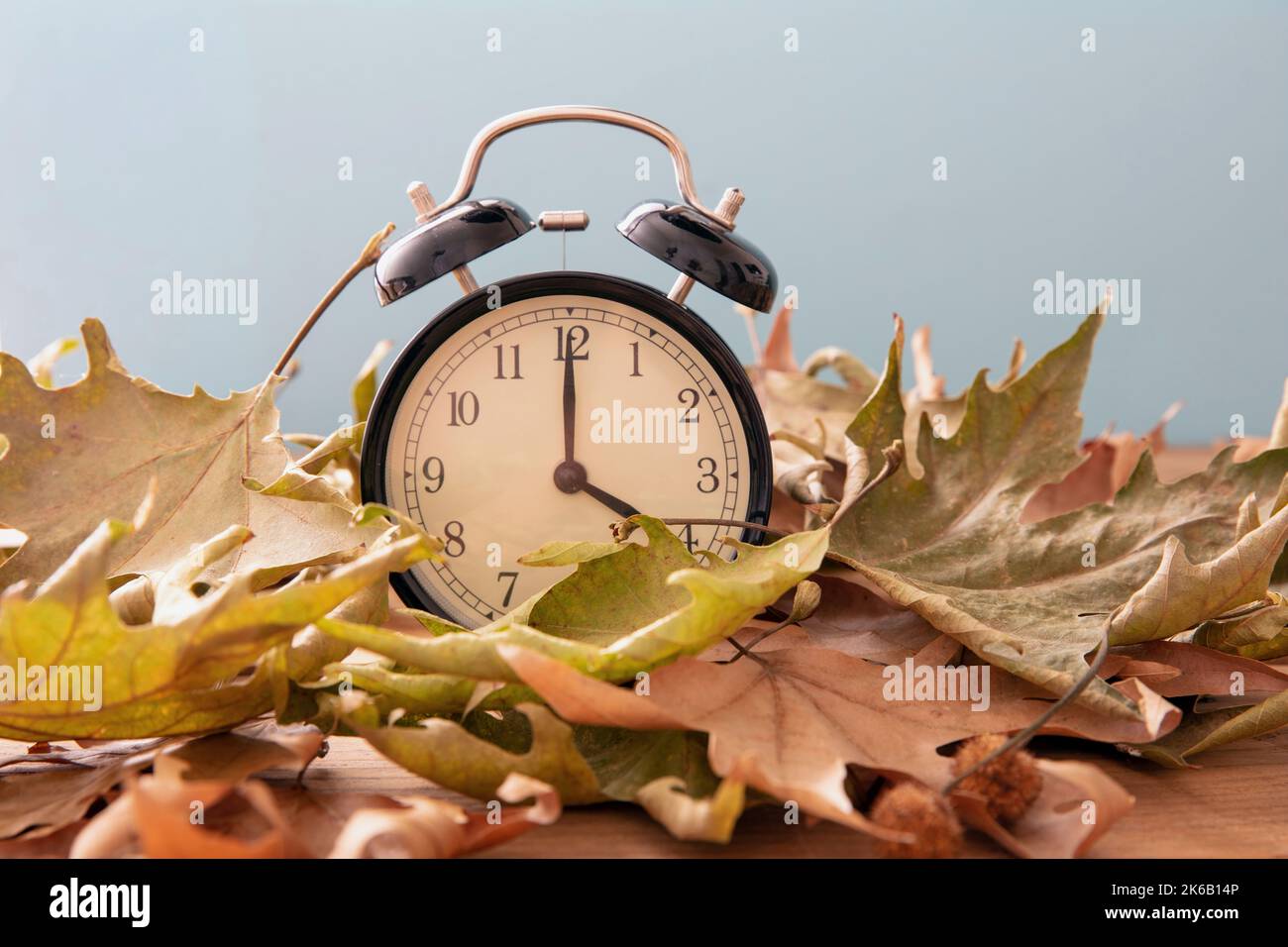 Rückfall Sommerzeit. Schwarzer Wecker und Herbstblätter auf Holztisch Stockfoto