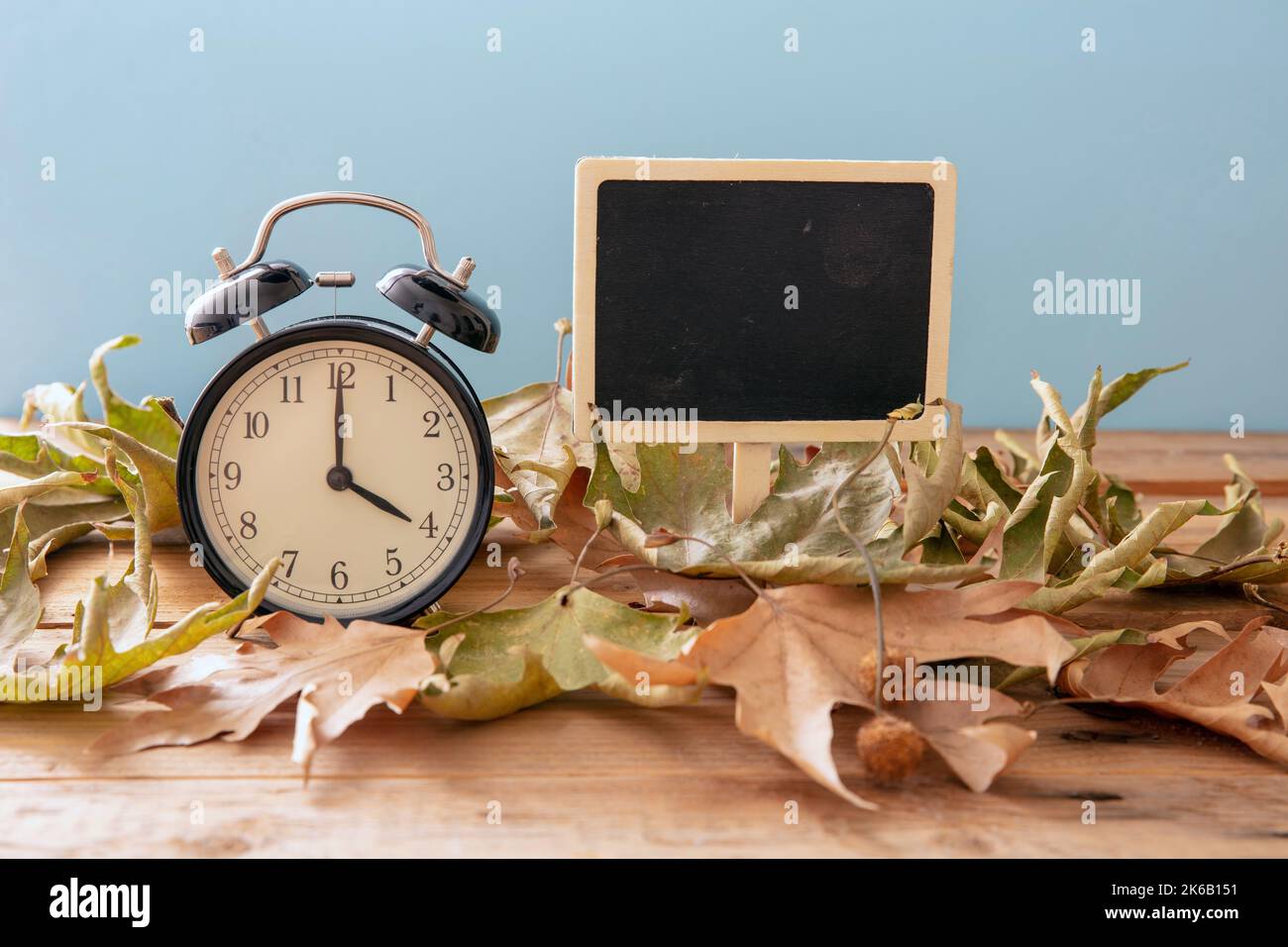 Rückfall Sommerzeit. Schwarzer Wecker und Herbstblätter auf Holztisch, Platz zum Kopieren Stockfoto