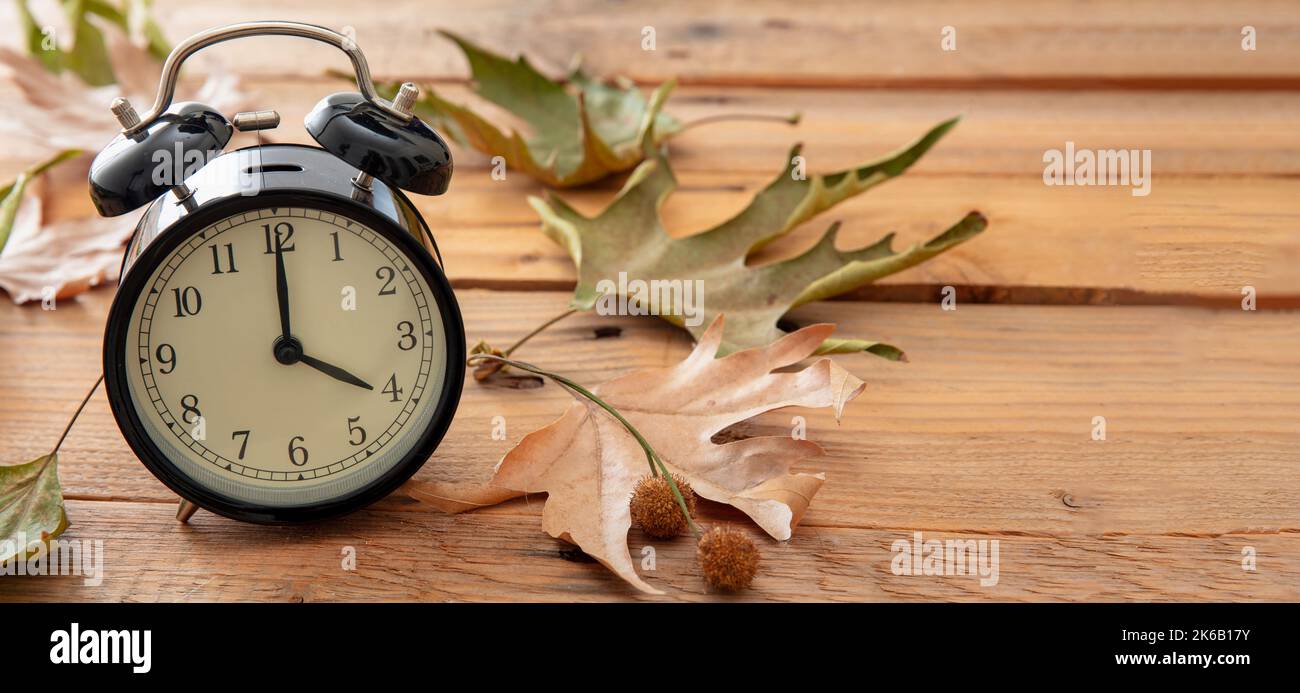 Sommerzeit, Fall Back. Schwarzer Wecker und Herbstblätter auf Holztisch, Platz zum Kopieren Stockfoto